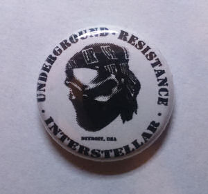UNDERGROUND RESISTANCE Metal Badge "INTERSTELLAR FUGITIVES" logo  (UNDERGROUND RESISTANCE)